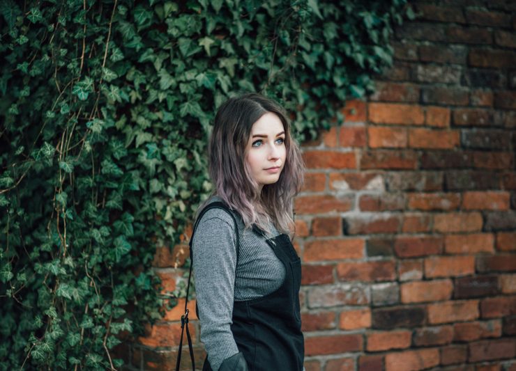girl stood in front of red brick wall wearing primark pinafore dress