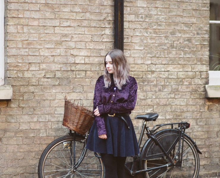girl stood in front of bicycle by a brick wall in cambridge, england