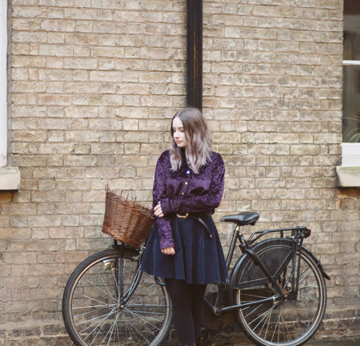 girl stood in front of bicycle by a brick wall in cambridge, england