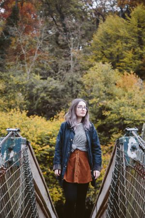 girl stood on bridge in front of autumn trees