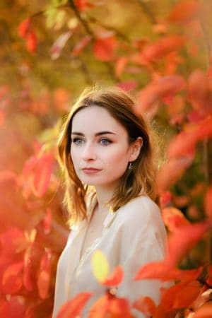 portrait of a girl wearing a silk shirt standing amongst autumn leaves. how to pose for photos