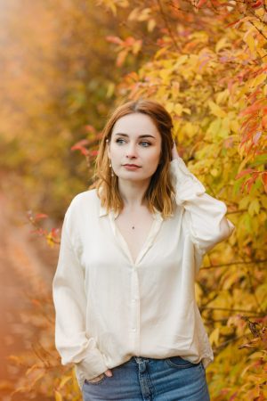 portrait of a girl wearing a silk shirt standing amongst autumn leaves. how to pose for photos