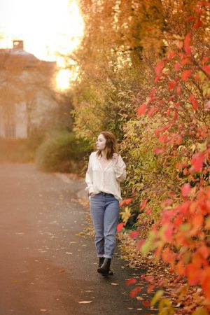 full length photo of a girl wearing a silk shirt and jeans standing amongst autumn leaves. how to pose for photos
