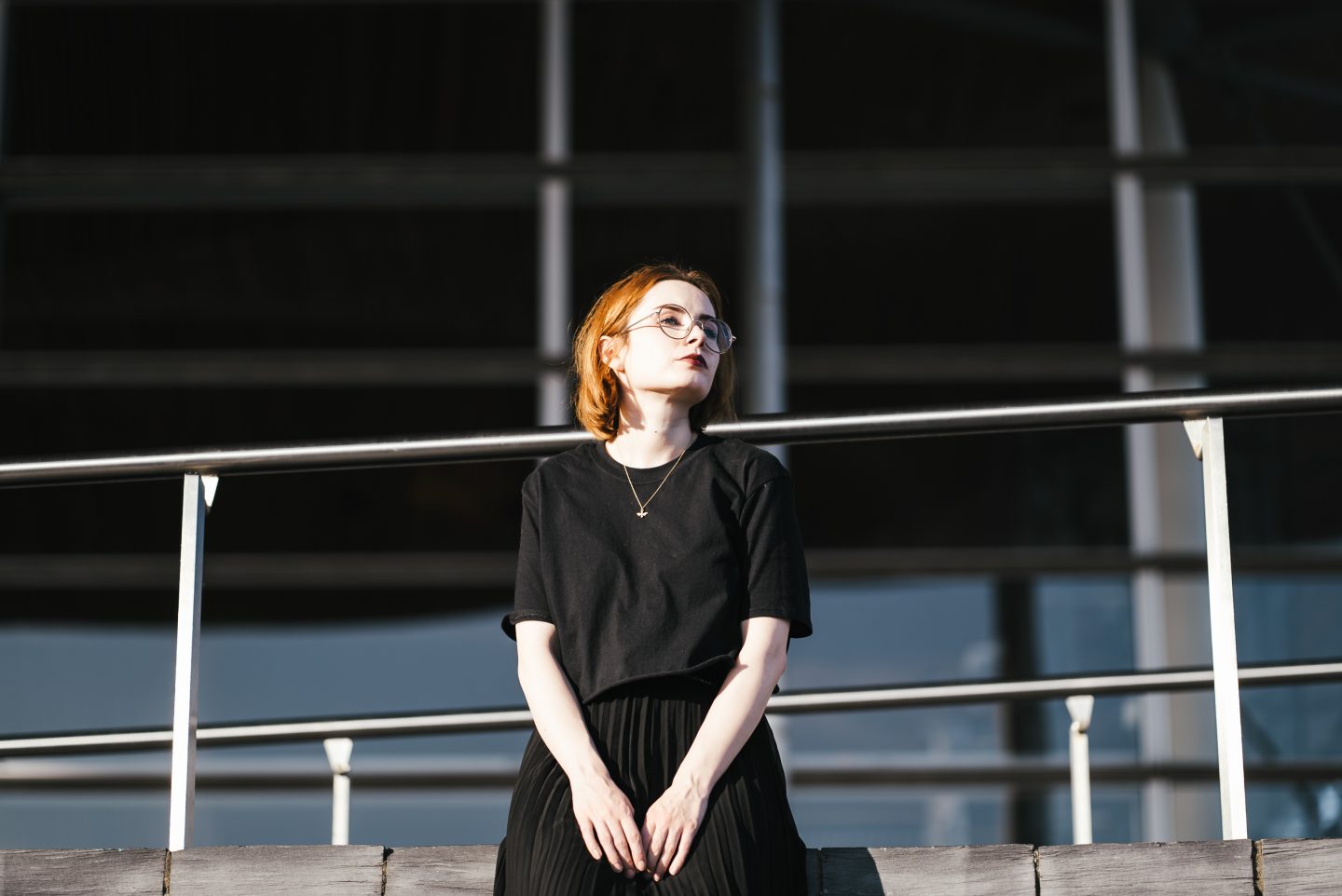girl wearing a black t shirt, black pleated skirt and gold bee necklace with short ginger hair and round glasses