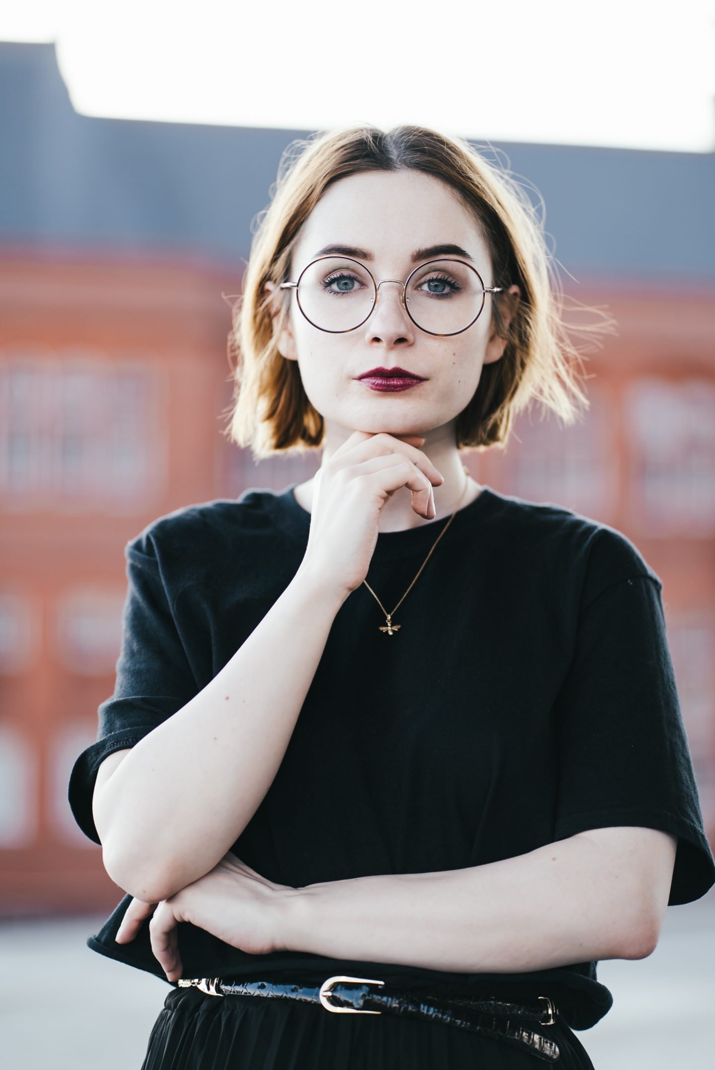 girl wearing a black t shirt and gold bee necklace with short ginger hair and round glasses