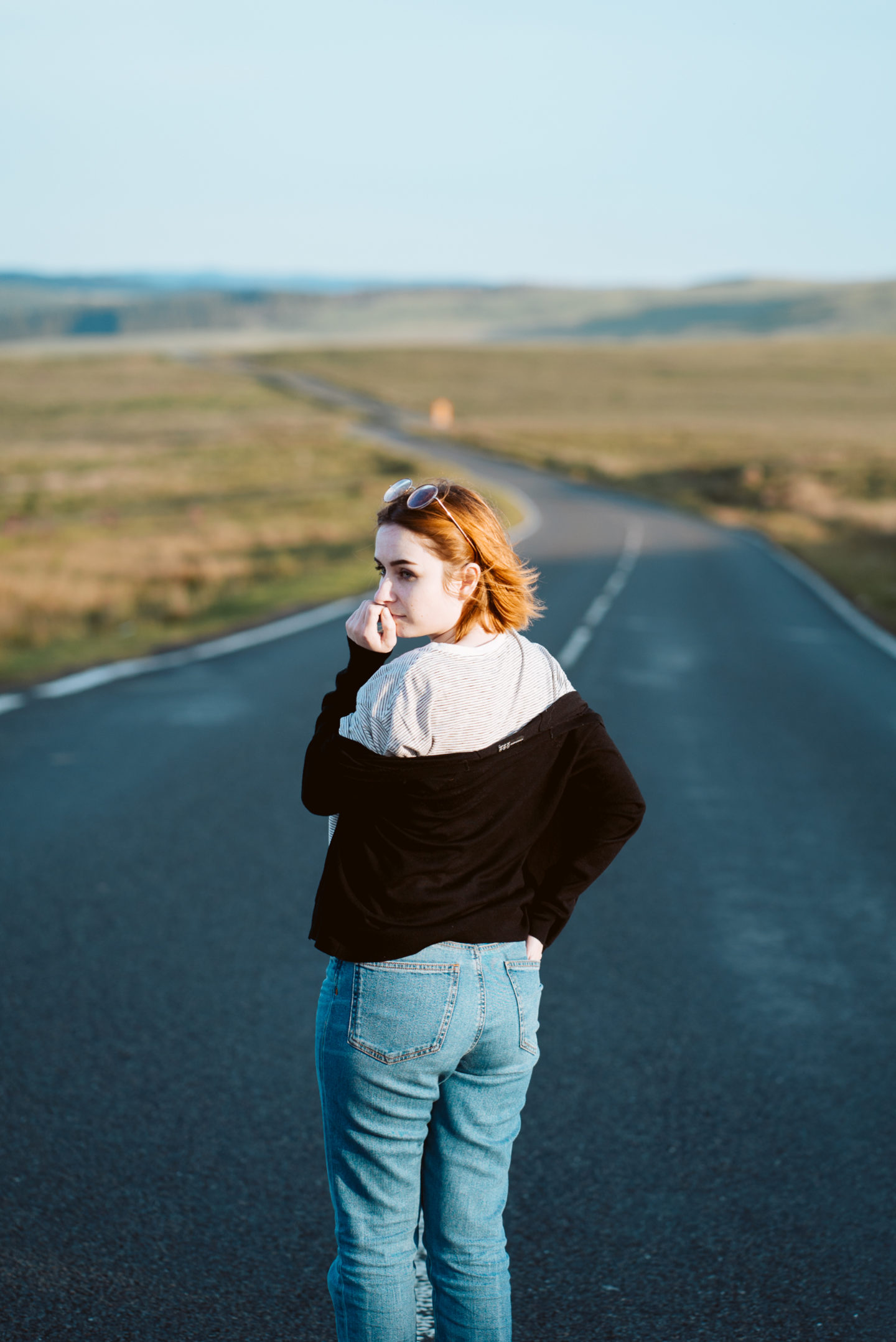 girl stood in the middle of a country road looking back to the camera surrounded by fields. Planning the best staycation for a cheap UK holiday