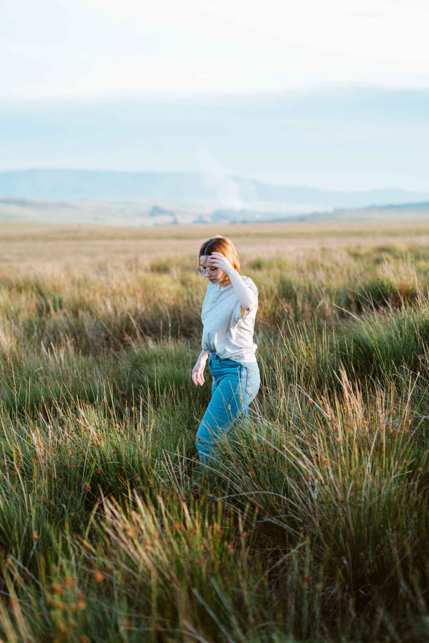 girl stood in field of long grass at sunset
