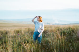 girl stood in field of long grass at sunset with hand to face to shield the sun. Planning the best staycation for a cheap UK holiday