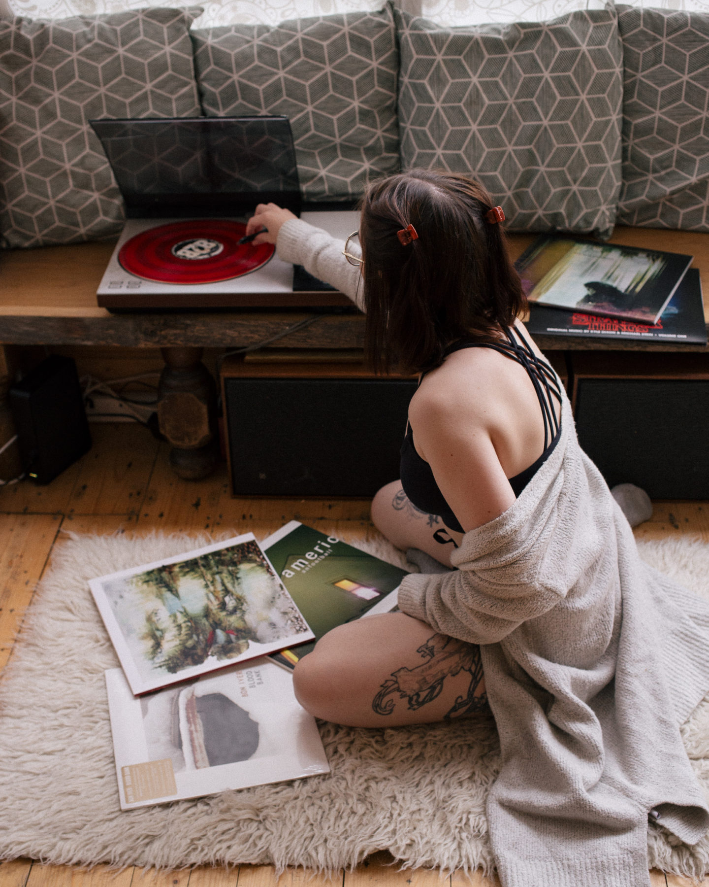 girl sitting on floor using a record player with records around her, wearing a crop top and oversized cardigan