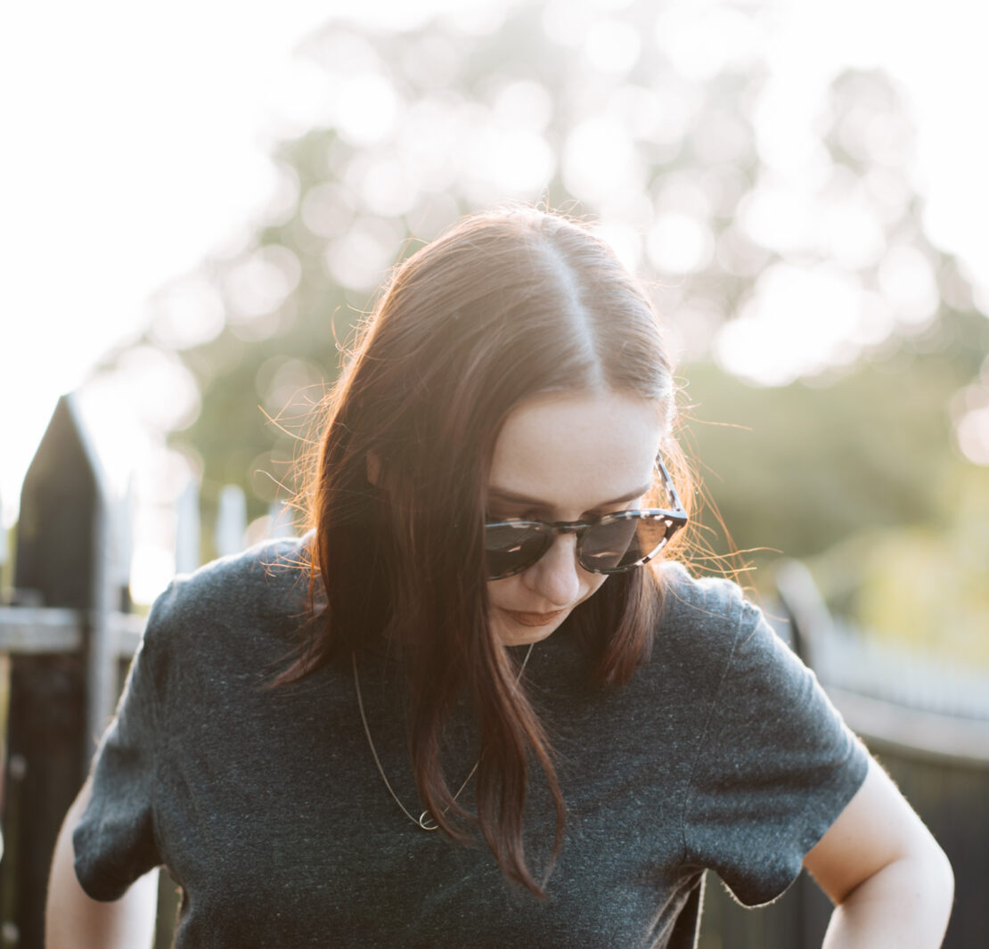 girl wearing sunglasses standing in street, backlit by the sun. Sustainable sunglasses pala eyewear