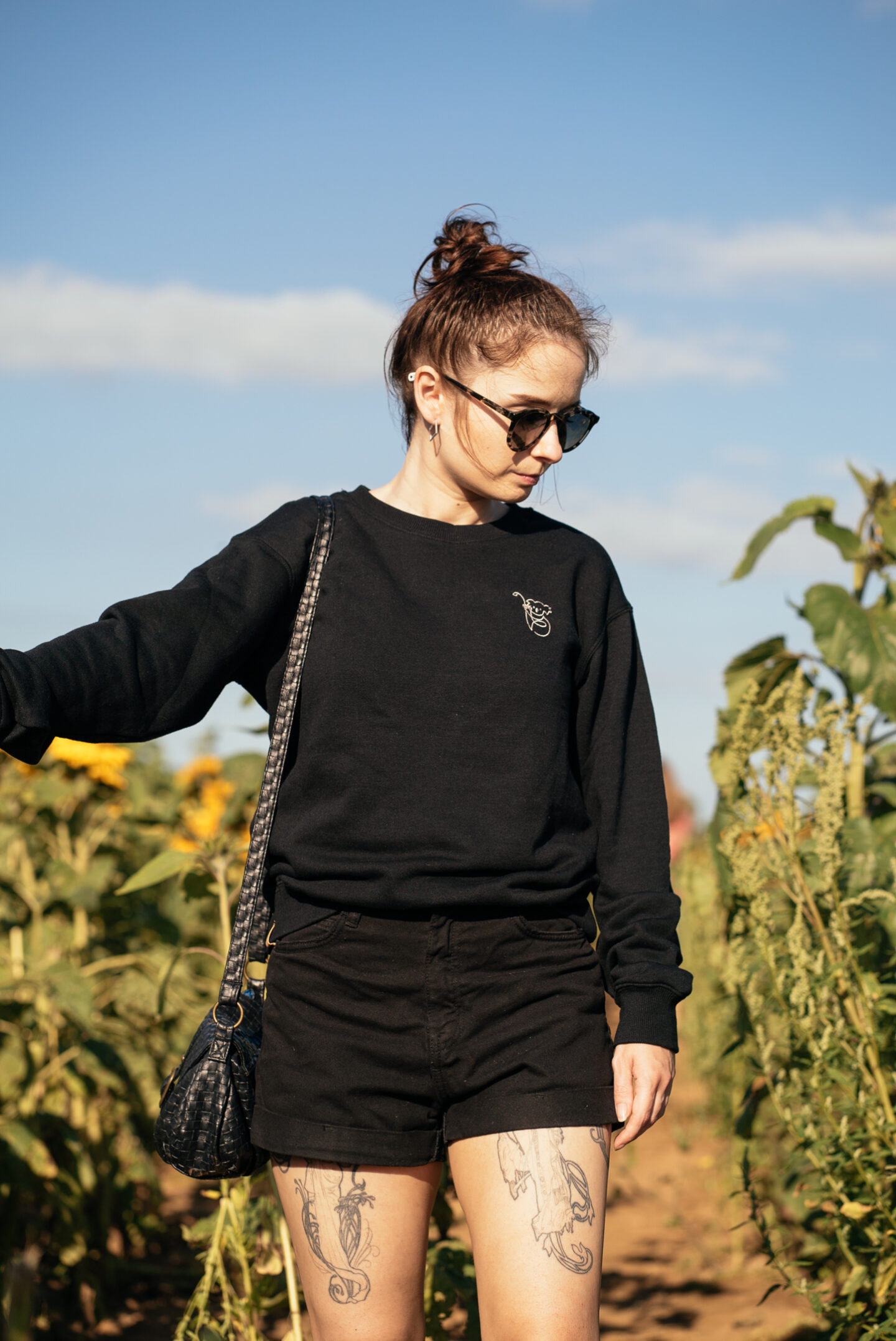 girl standing in a sunflower field at sunset wearing sunglasses, a black jumper and black shorts. Tips for a sustainable wardrobe